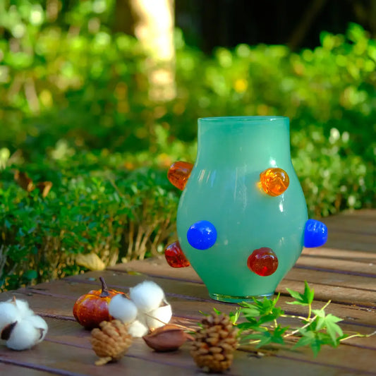 Petit vase en verre soufflé vert décoré de pastilles bleues et ambrées, parfait pour une touche artistique.