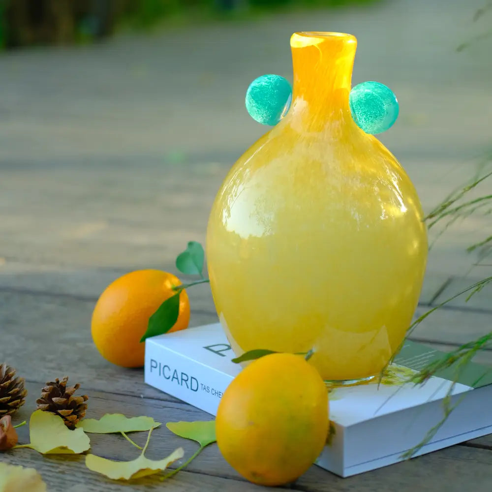 Vase jaune en verre soufflé artisanal, silhouette bombée et détails verts inspirés de la nature.
