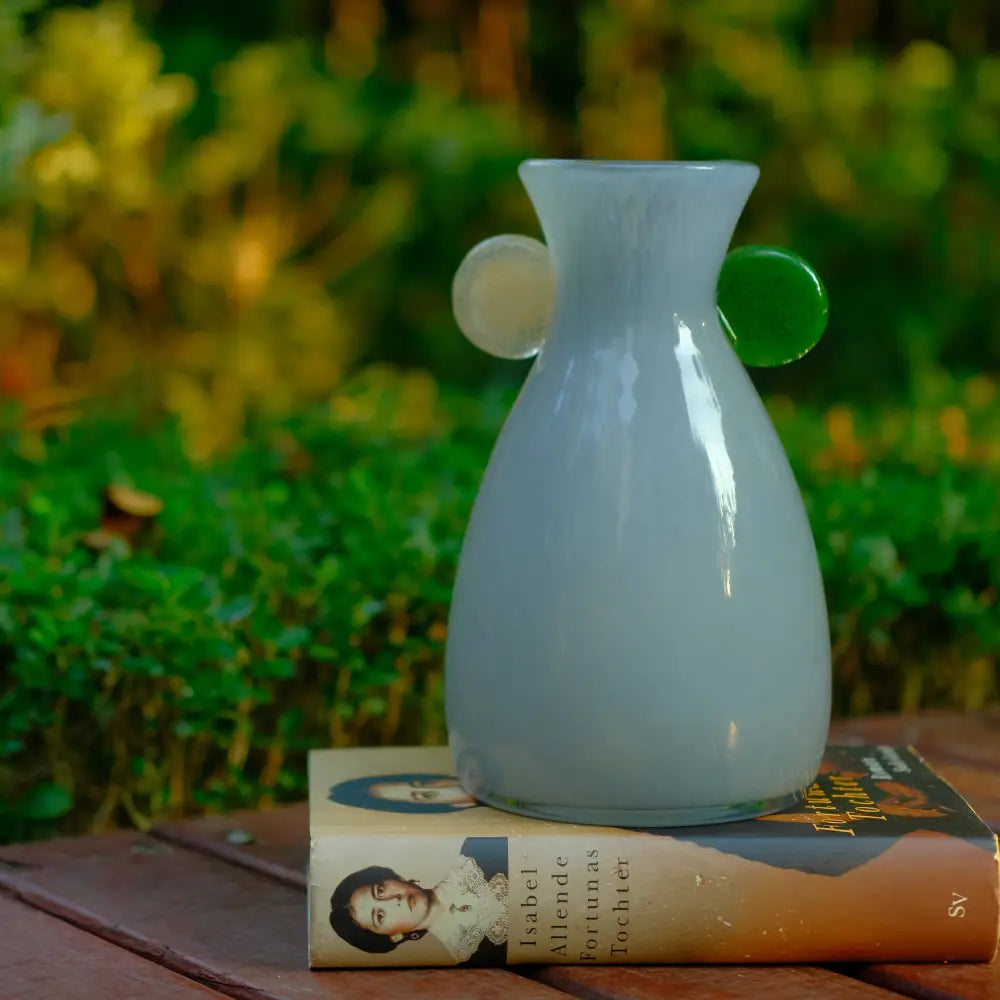 Décorer vase artisanal aux tons gris doux, posé sur un livre dans un décor naturel.