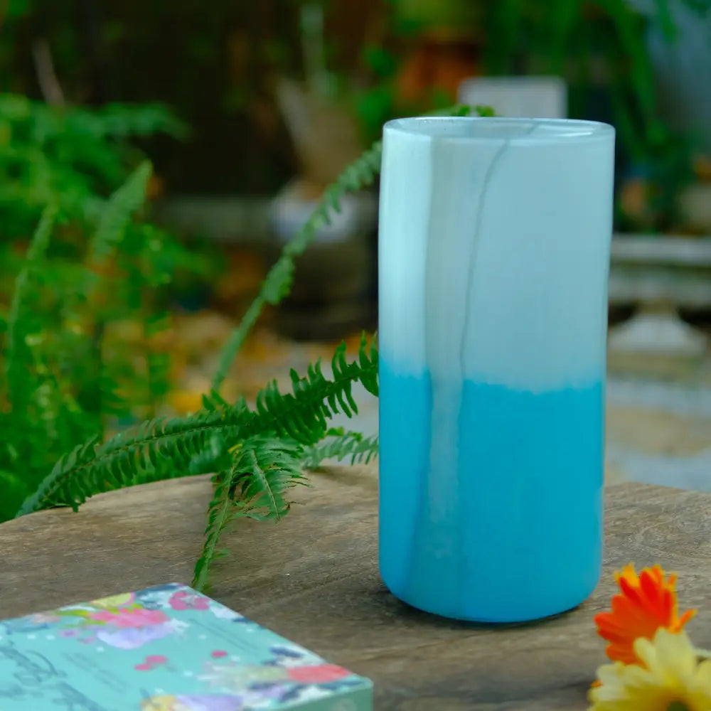 Design vase en forme de cylindre, finition bleu lagon, posé en extérieur sur une table en bois.