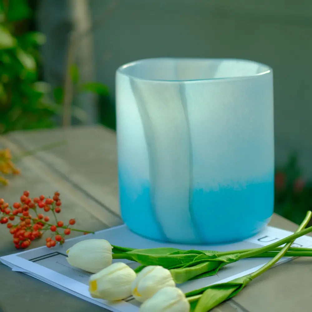 Design vase cylindrique aux tons bleu océan, présenté avec des tulipes blanches.
