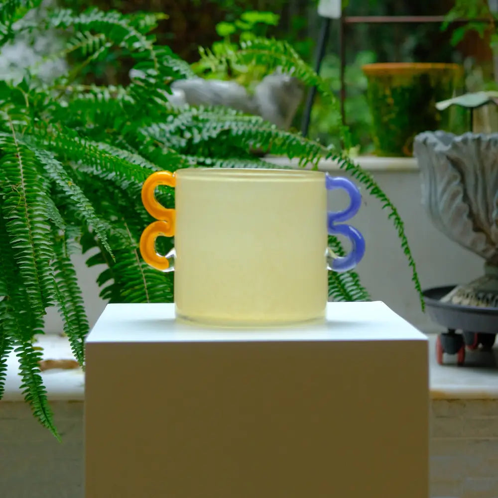 Mini vase en verre beige avec poignées colorées, design original et artisanal.