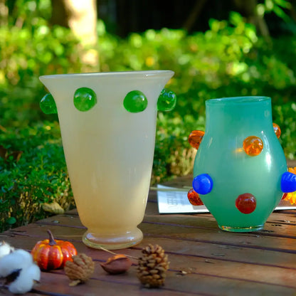 Petit vase en verre soufflé artisanal avec détails bleus et ambrés, posé dans un décor naturel en extérieur.