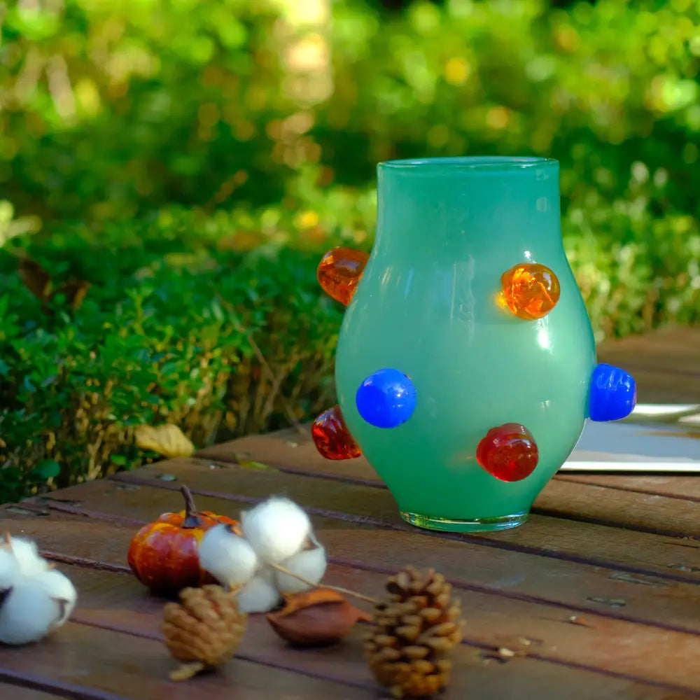 Petit vase en verre soufflé vert clair, rehaussé de motifs arrondis multicolores pour un style ludique.