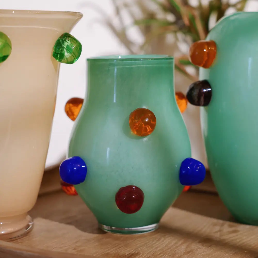 Petit vase en verre vert orné de pastilles colorées bleu et ambre, au style ludique et moderne pour la décoration intérieure.