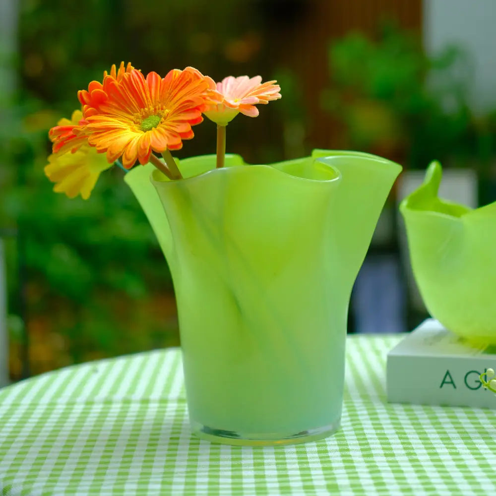 Petit vase en verre vert dégradé, au design ondulé et délicat.