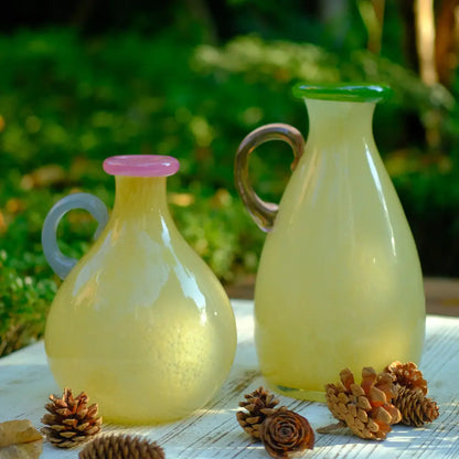 Petit vase jaune en verre soufflé avec poignée colorée, pièce élégante et moderne.