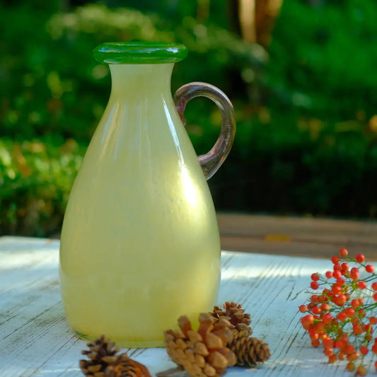Petit vase en verre pastel doté d’une anse rosée et d’un bord vert, parfait pour une déco délicate.