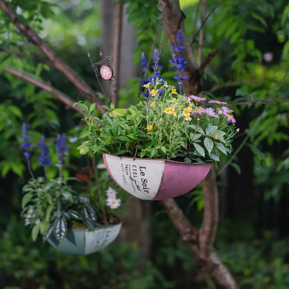 Pot de fleur à suspendre – Demi-umbrella en métal vieilli, rempli de fleurs colorées, suspendu à un arbre.