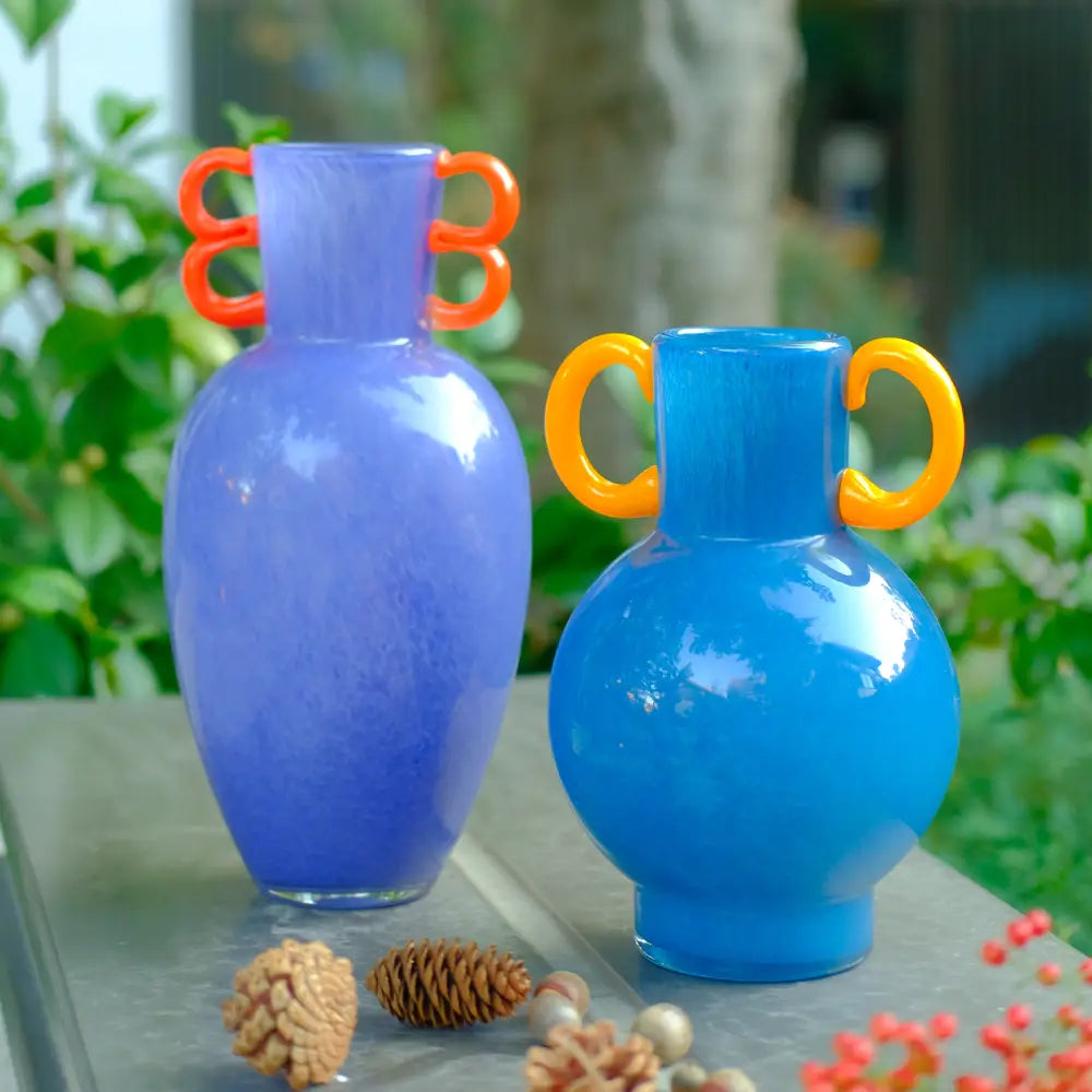 Vase déco amphore en verre soufflé d’un bleu profond, orné de poignées circulaires jaunes.