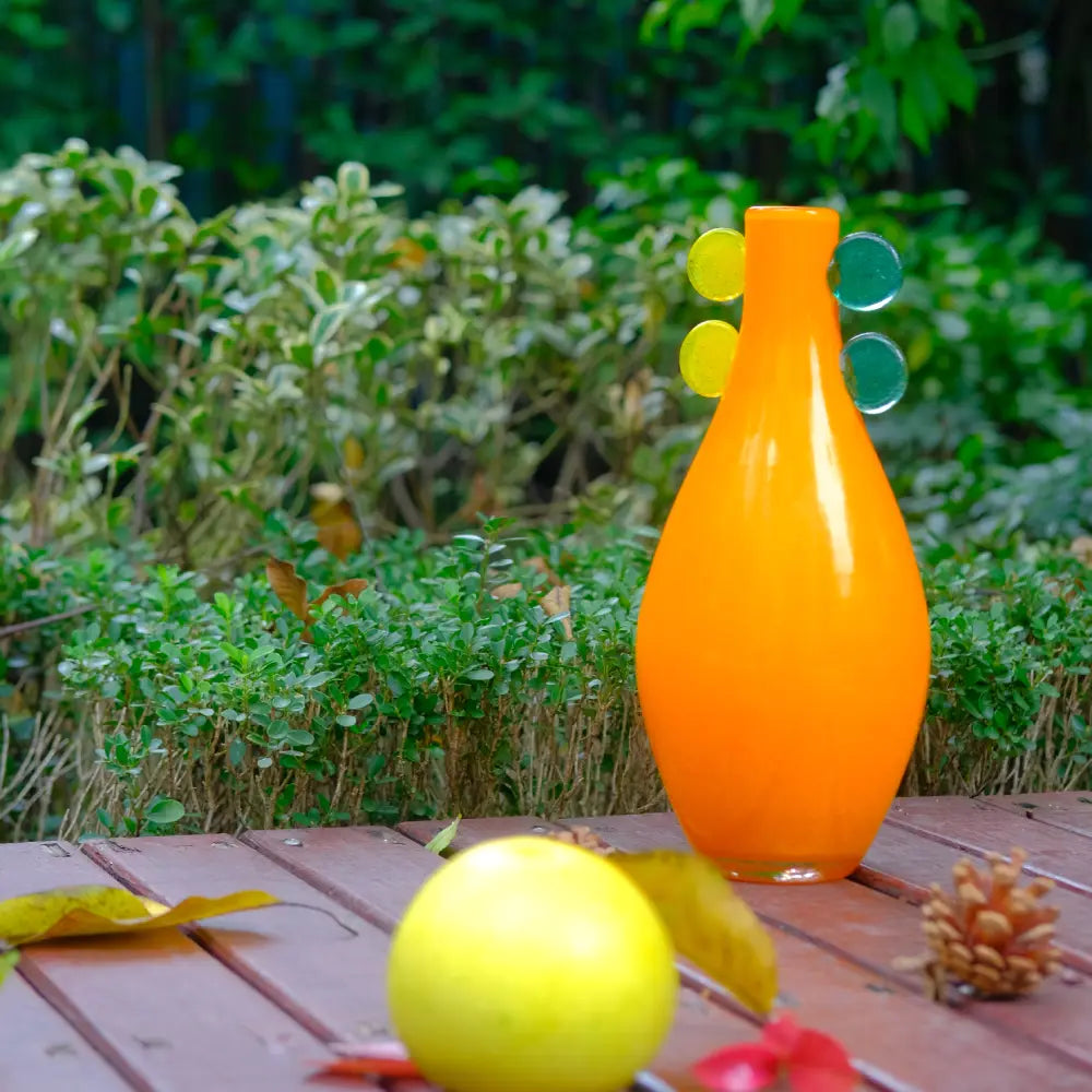 Vase orange en verre soufflé à la main, orné de pastilles vertes et jaunes.