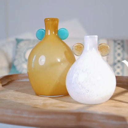 Vase jaune en verre soufflé avec deux anses rondes bleues, au design moderne et raffiné.