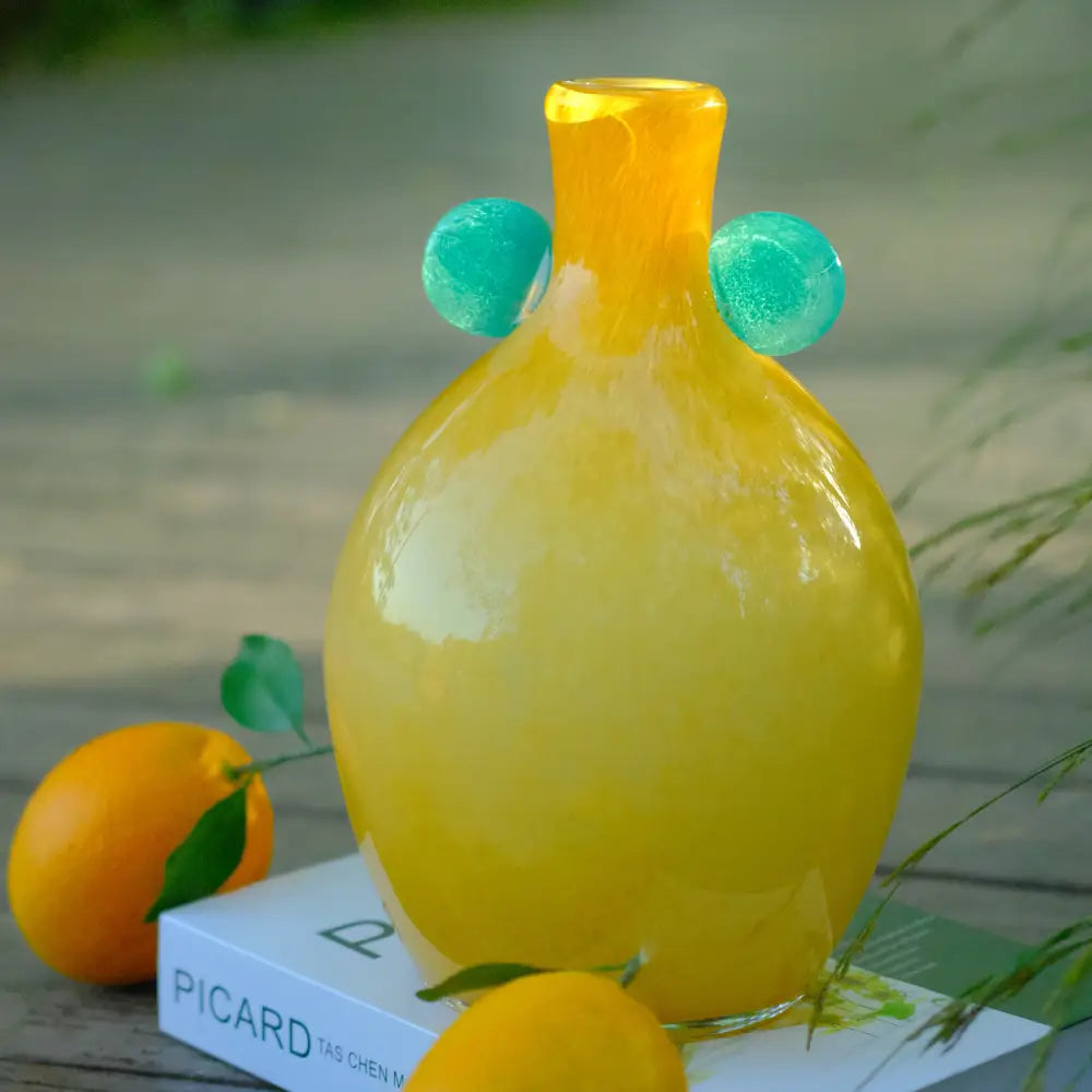 Vase jaune en verre soufflé aux nuances miel, décoré d’oreilles vertes pour une touche contemporaine.