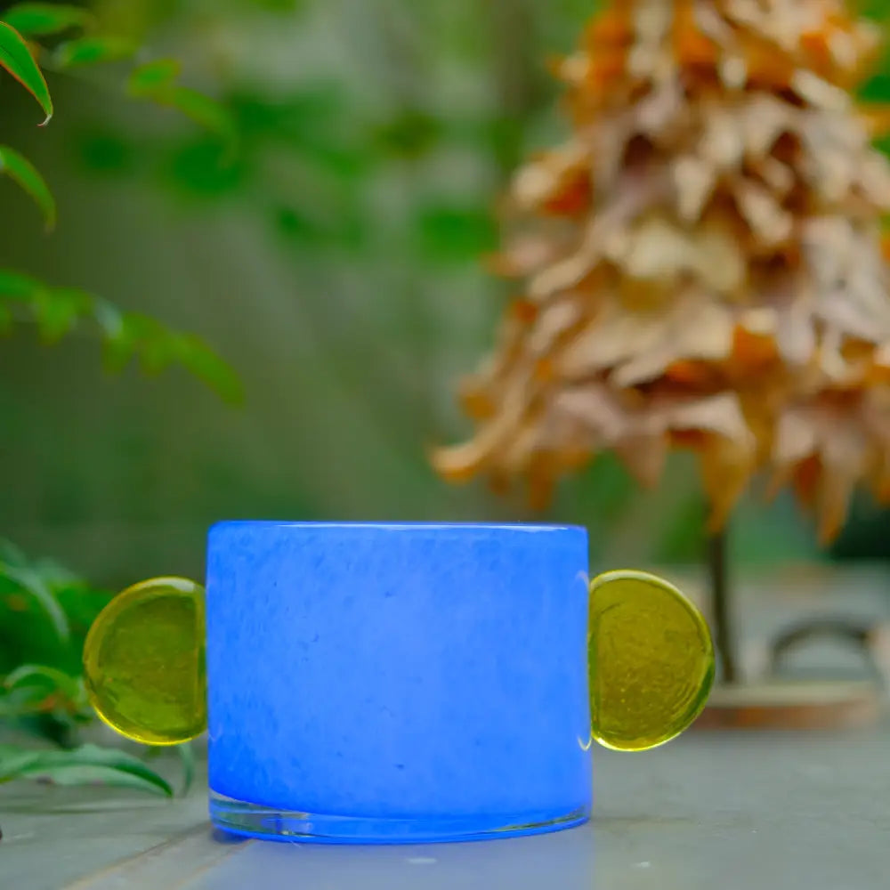 Vase bleu en verre soufflé, orné de disques jaunes, idéal pour bougie ou fleurs.