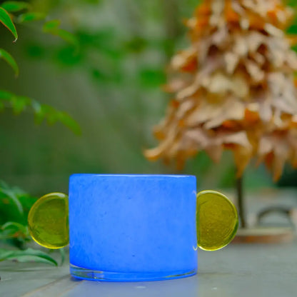 Vase bleu en verre soufflé, orné de disques jaunes, idéal pour bougie ou fleurs.
