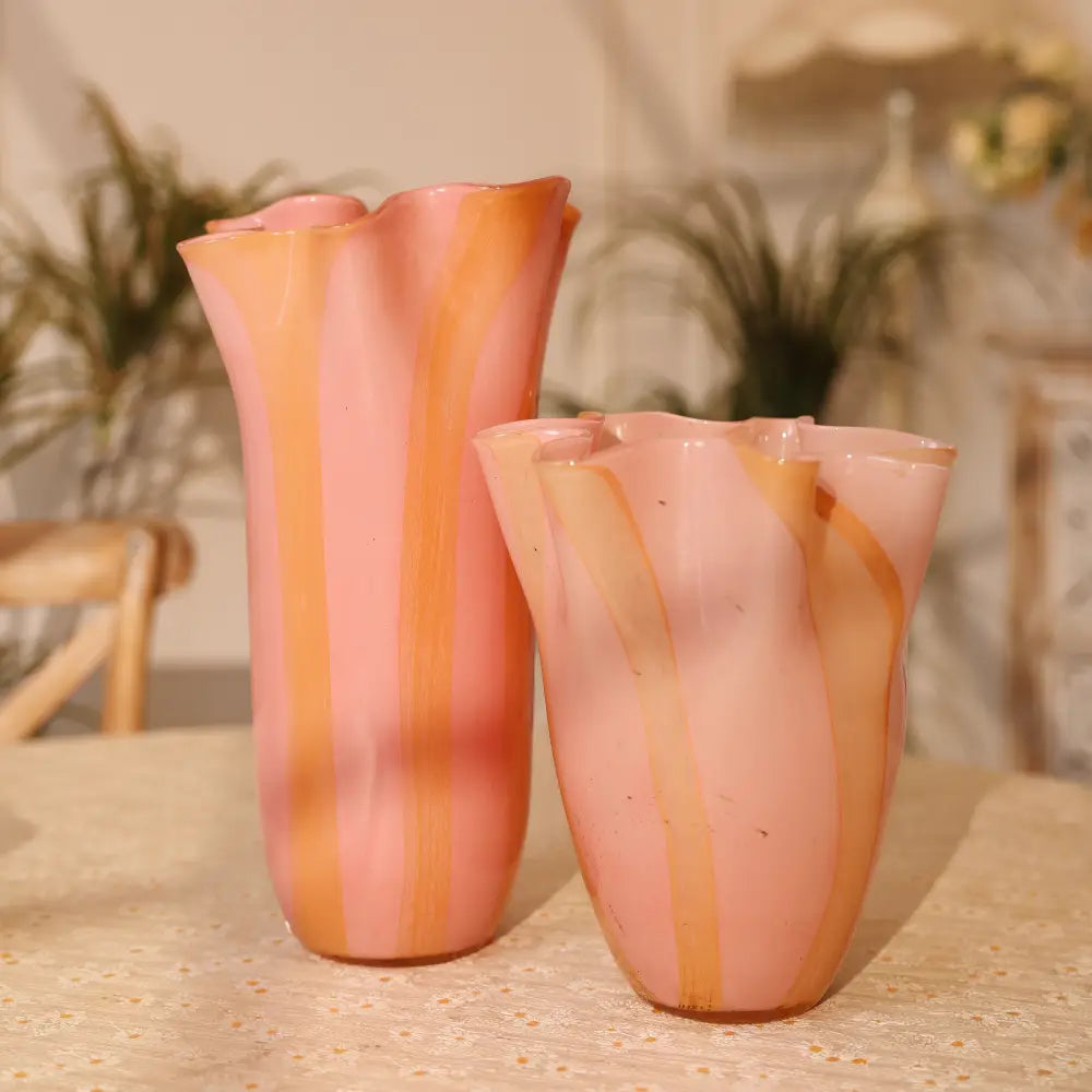 Vase design en verre soufflé aux teintes rose et ambre, au col ondulé inspiré des fleurs.