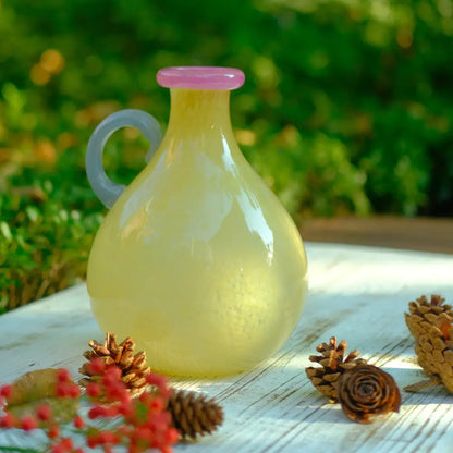Vase soliflore en verre soufflé jaune avec anse noire et col rose, au design artisanal.