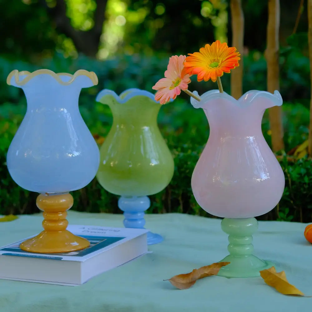 Vase with design en verre soufflé pastel avec bord en forme de pétales, présenté en extérieur.