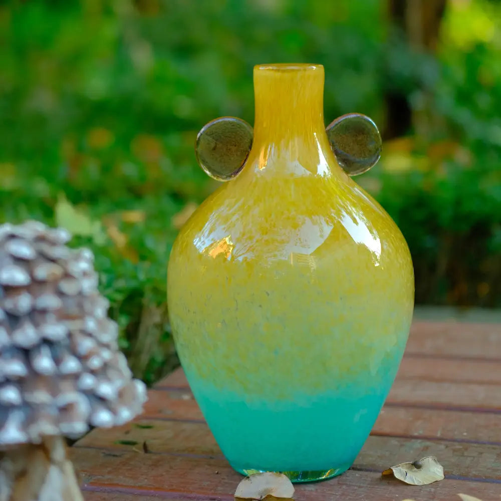 Vase boule en verre soufflé au dégradé jaune et bleu, orné de pastilles rosées sur les côtés.